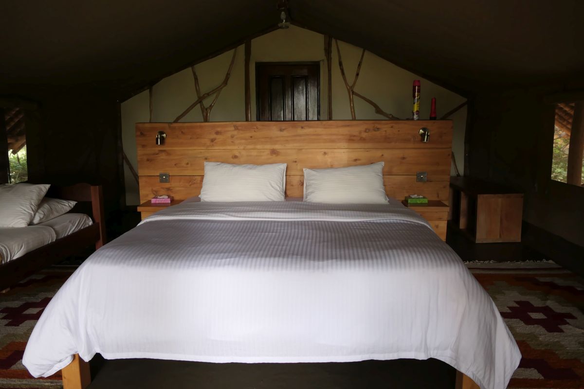 Großes Bett in einem Safari-Zelt des Satao Camp mit schlichter Holzeinrichtung und gemütlicher Atmosphäre.