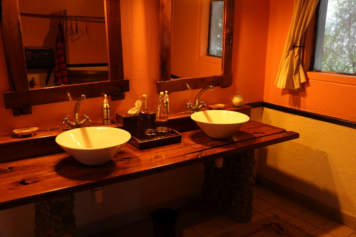 Badezimmer im Tipilikwani Mara Camp mit zwei Waschbecken auf einem rustikalen Holzwaschtisch.