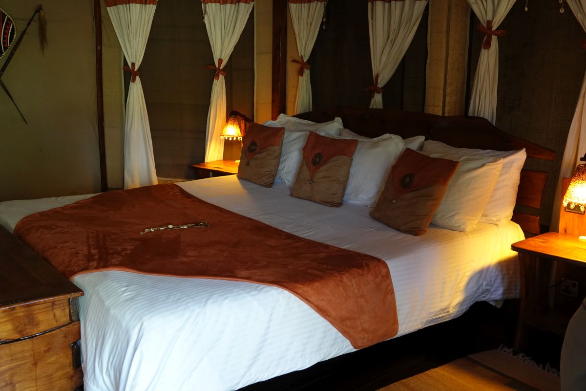 Komfortables Doppelbett in einem Safari-Zelt des Tipilikwani Mara Camps mit stimmungsvoller Beleuchtung.