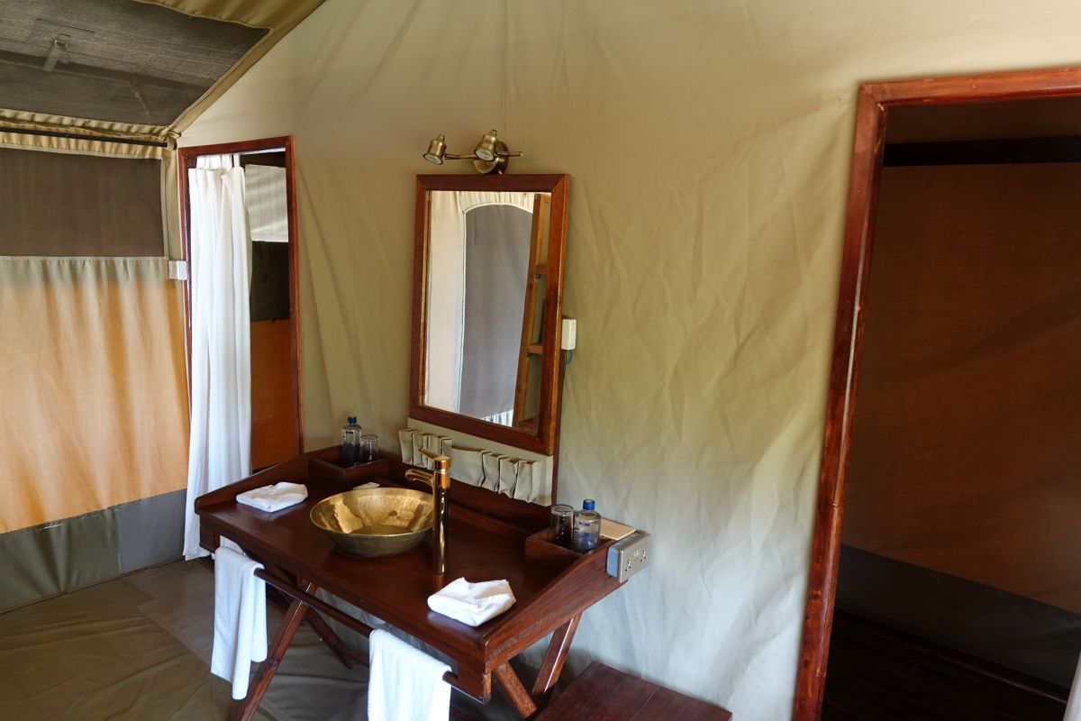 Waschbereich im Safari-Zelt des Elatia Mara Camp mit Holzwaschtisch, Spiegel und natürlicher Einrichtung.