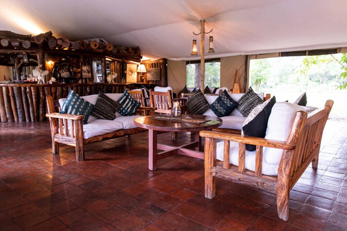 Gemütlicher Lounge-Bereich im Governors Camp mit rustikalen Holzmöbeln und offenem Blick ins Grüne.