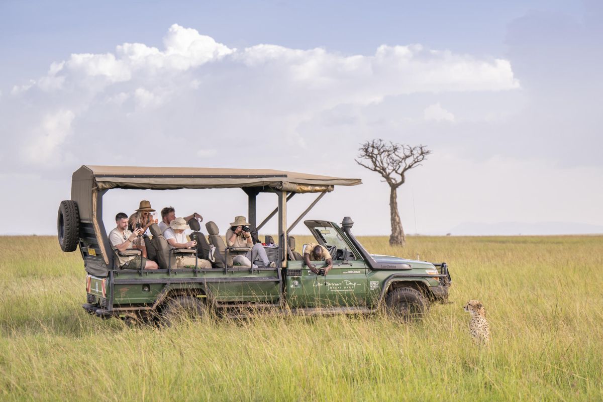 Safari-Fahrzeug mit Gästen während einer Pirschfahrt durch die offene Savanne der Masai Mara.