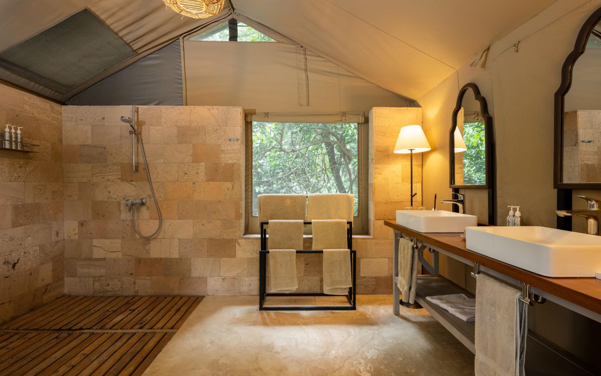 Modernes Badezimmer im Governors Camp mit Naturstein-Dusche, Doppelwaschbecken und großem Fensterblick ins Grüne.