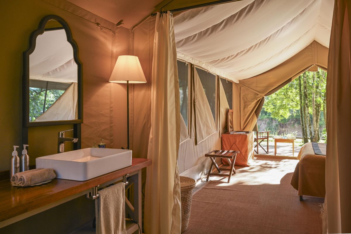 Innenbereich eines Safari-Zelts im Governors Camp mit Waschbereich, gemütlichem Bett und offenem Blick ins Grüne.