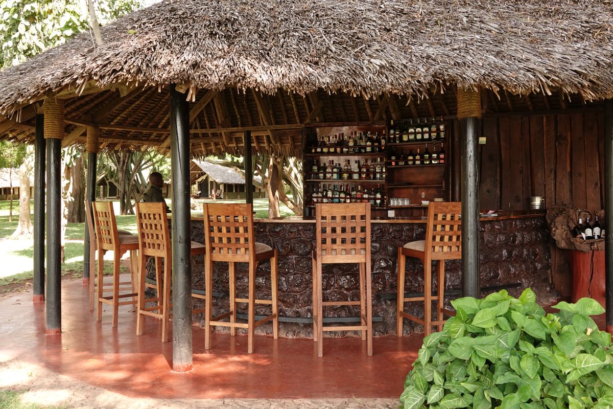 Offene Bar mit Reetdach und hohen Holzstühlen.