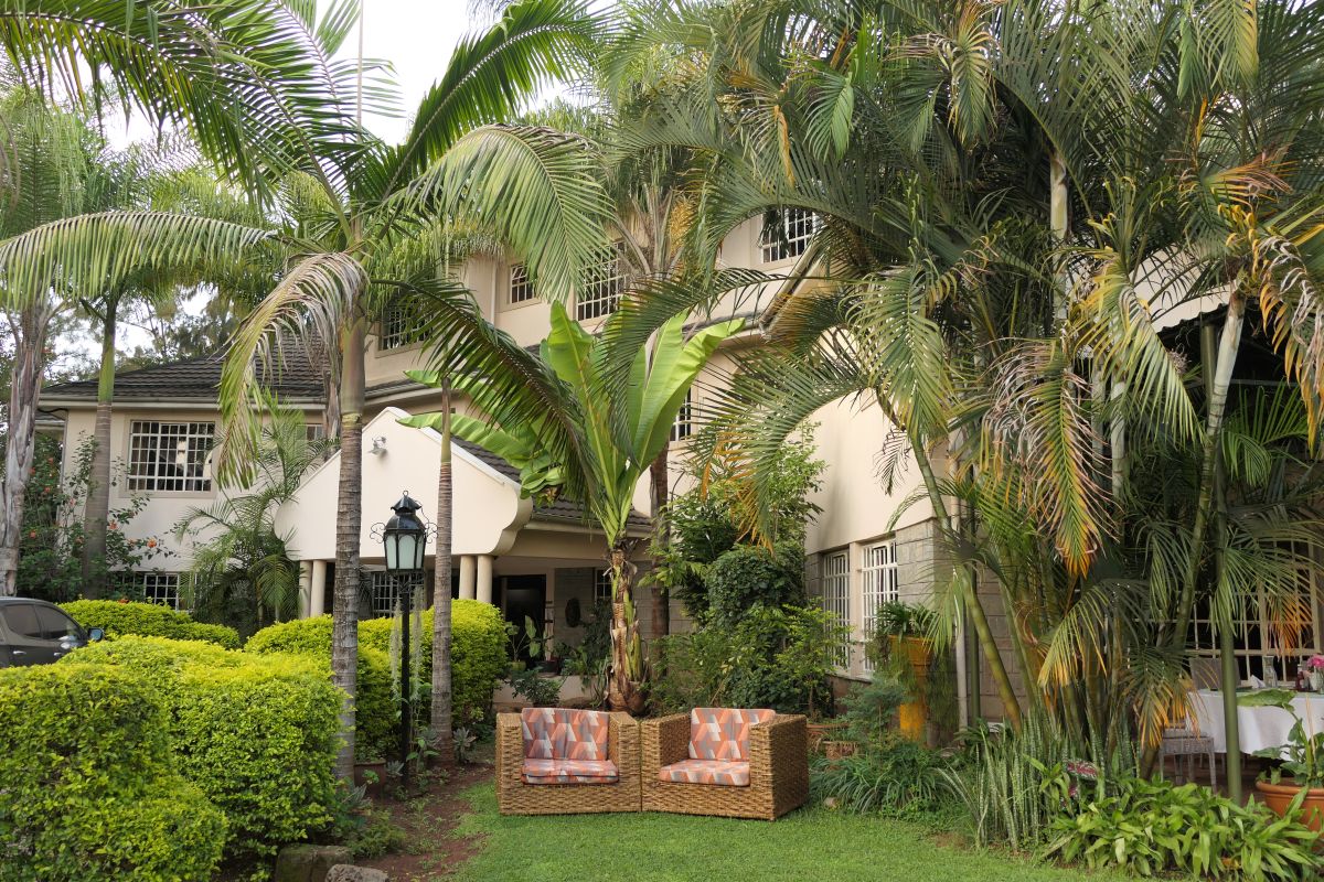 Vorderseite von Hotel Rudi mit vielen Palmen und Garten mit zwei Sesseln