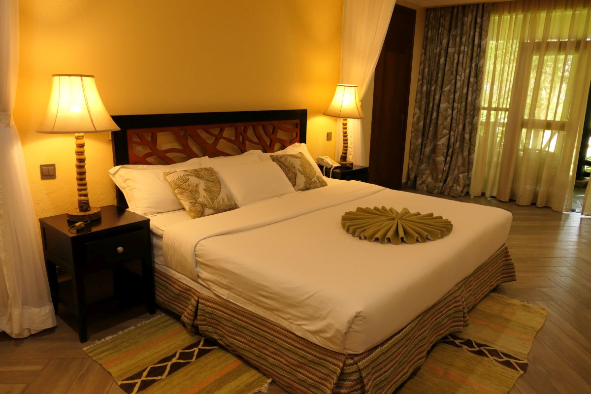 Modern eingerichtetes Gästezimmer der Sawela Lodge mit großem Doppelbett, Nachttischen, warmem Licht und Zugang zu einem Balkon oder einer Terrasse.