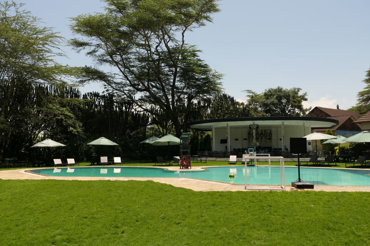 Großer Außenpool der Sawela Lodge mit Liegestühlen, Sonnenschirmen und gepflegten Grünflächen, umgeben von Bäumen und tropischer Vegetation.