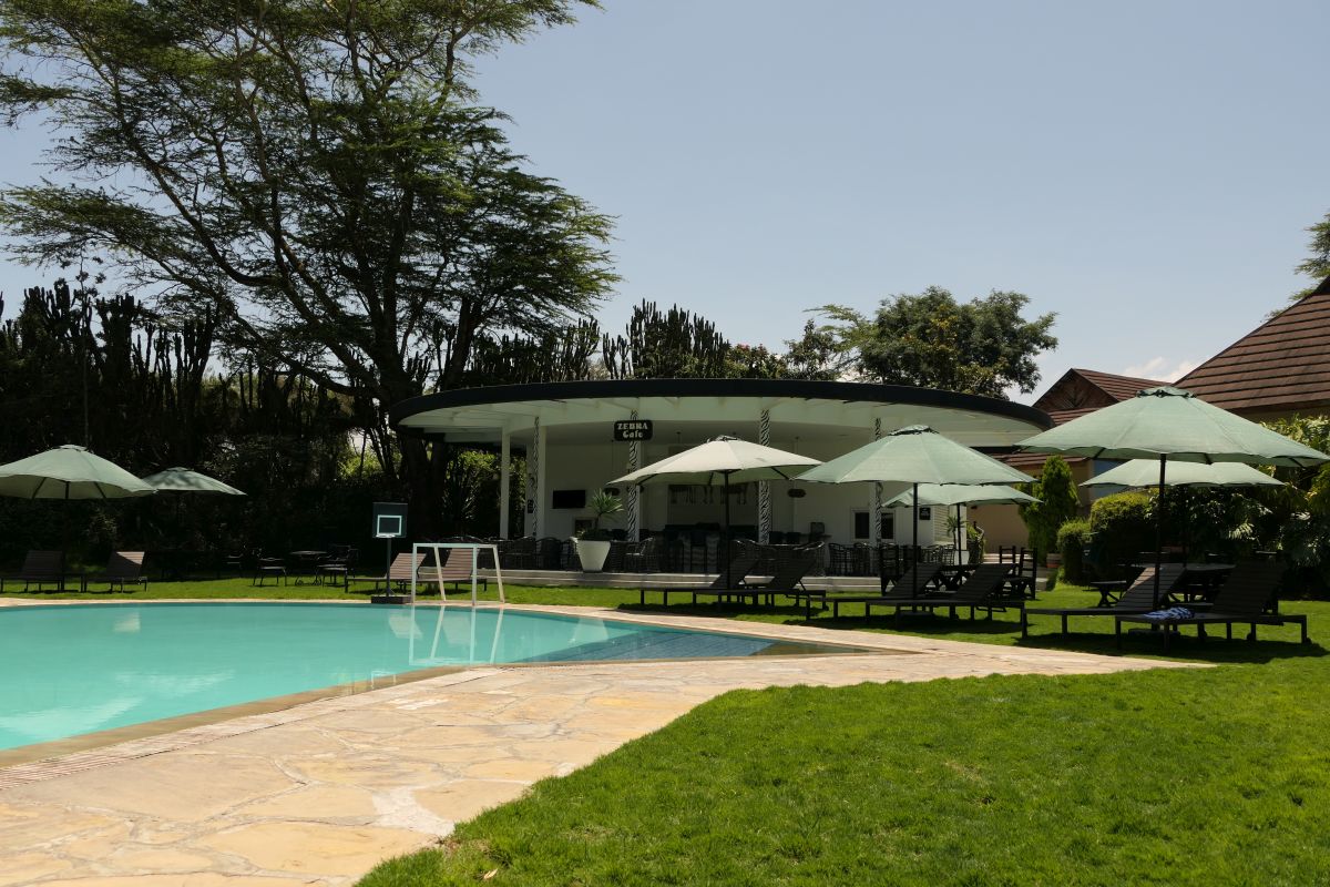 Großer Swimmingpool der Sawela Lodge mit Sonnenschirmen, Liegestühlen und gepflegten Grünflächen, umgeben von Bäumen und den Gebäuden der Lodge.