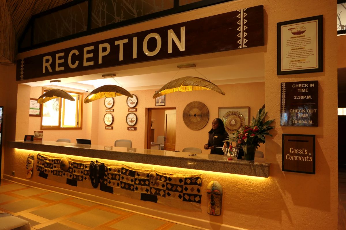Freundlich gestaltete Rezeption der Sawela Lodge mit langer Empfangstheke, dekorativen Elementen, Informationsanzeigen und warmem Licht.