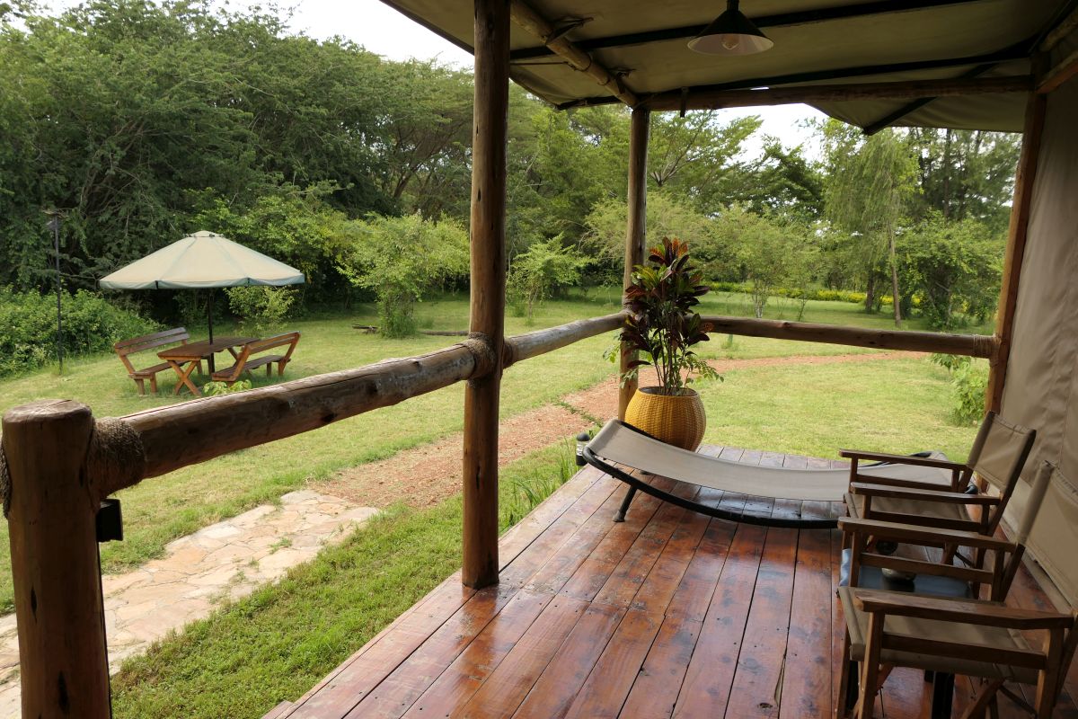 Holzveranda am Zelt mit Liege und Safari-Stühlen mit Blick auf Wiese und Buschland und einer Sitzgruppe