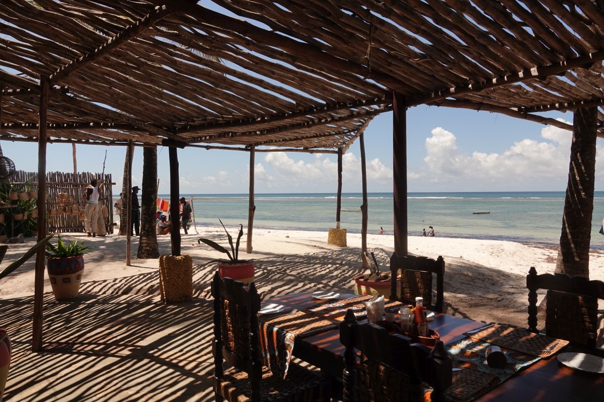 Tische und Stühle unter einer Holz-Pergola mit Blick aufs Meer