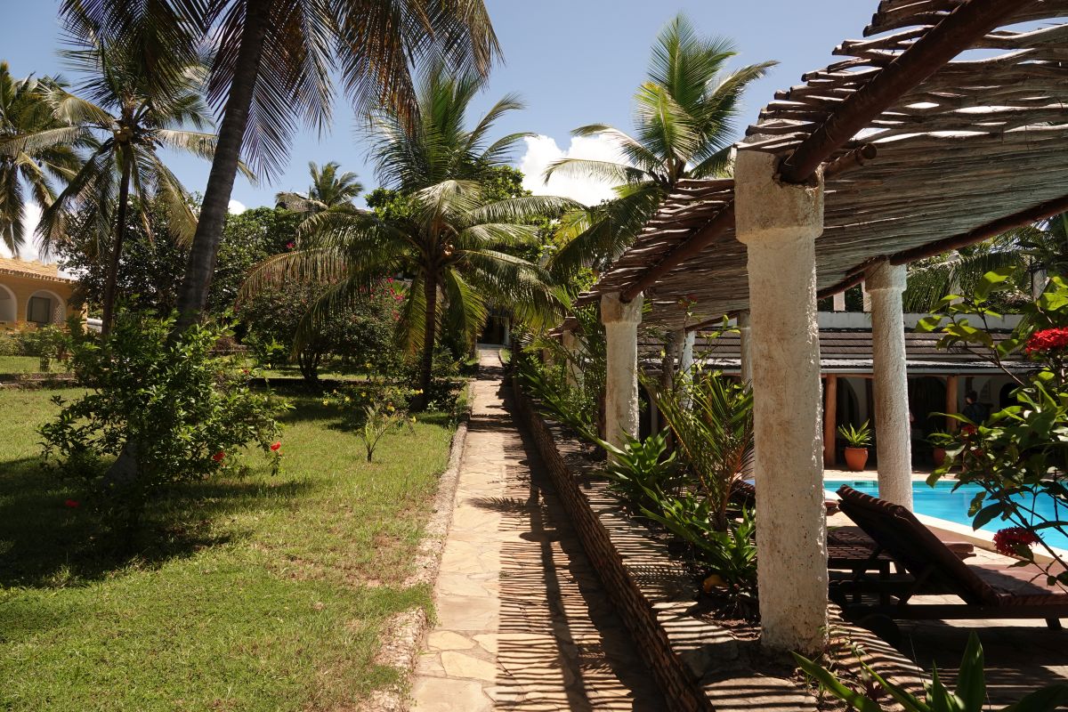 Weg durch Hotelanlage Coconut Beach Lodge mit gepflegtem Garten und Pool mit Liegen